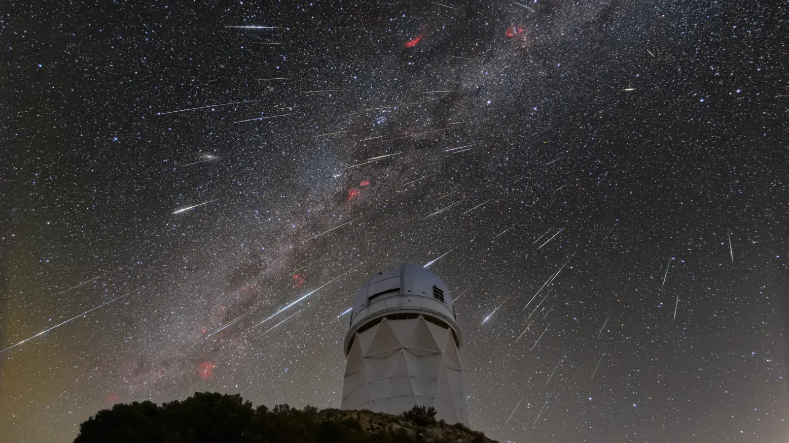 Dozens of Geminid meteor streaks and the Milky Way above the white dome of a telescope at Kitt Peak National Observatory in Arizona, a stack of photos taken over about two hours at the December 2023 peak