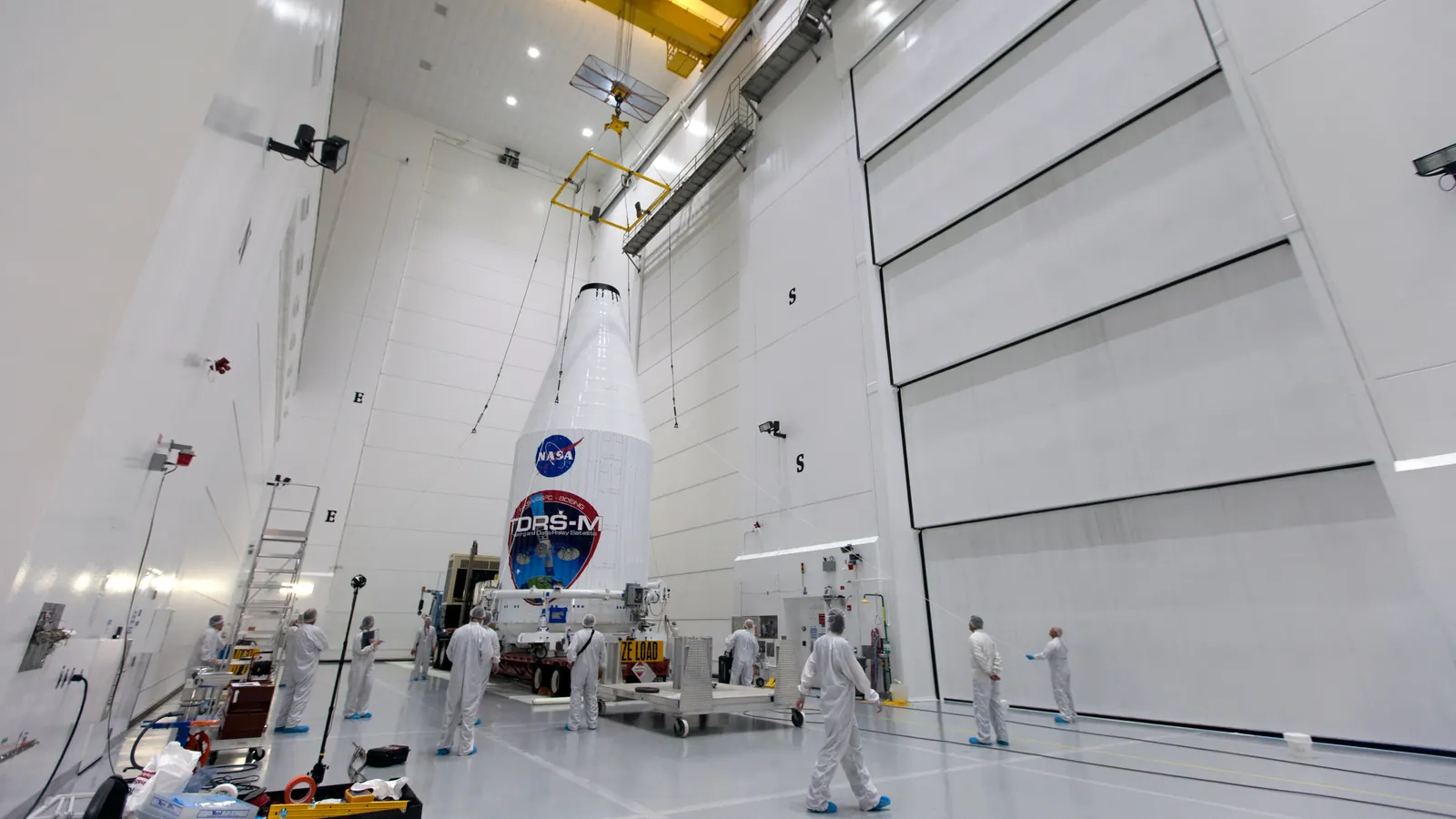 NASA's TDRS-M relay satellite, bound for geostationary orbit, sealed inside its payload fairing and hoisted in a tall white processing facility in August 2017