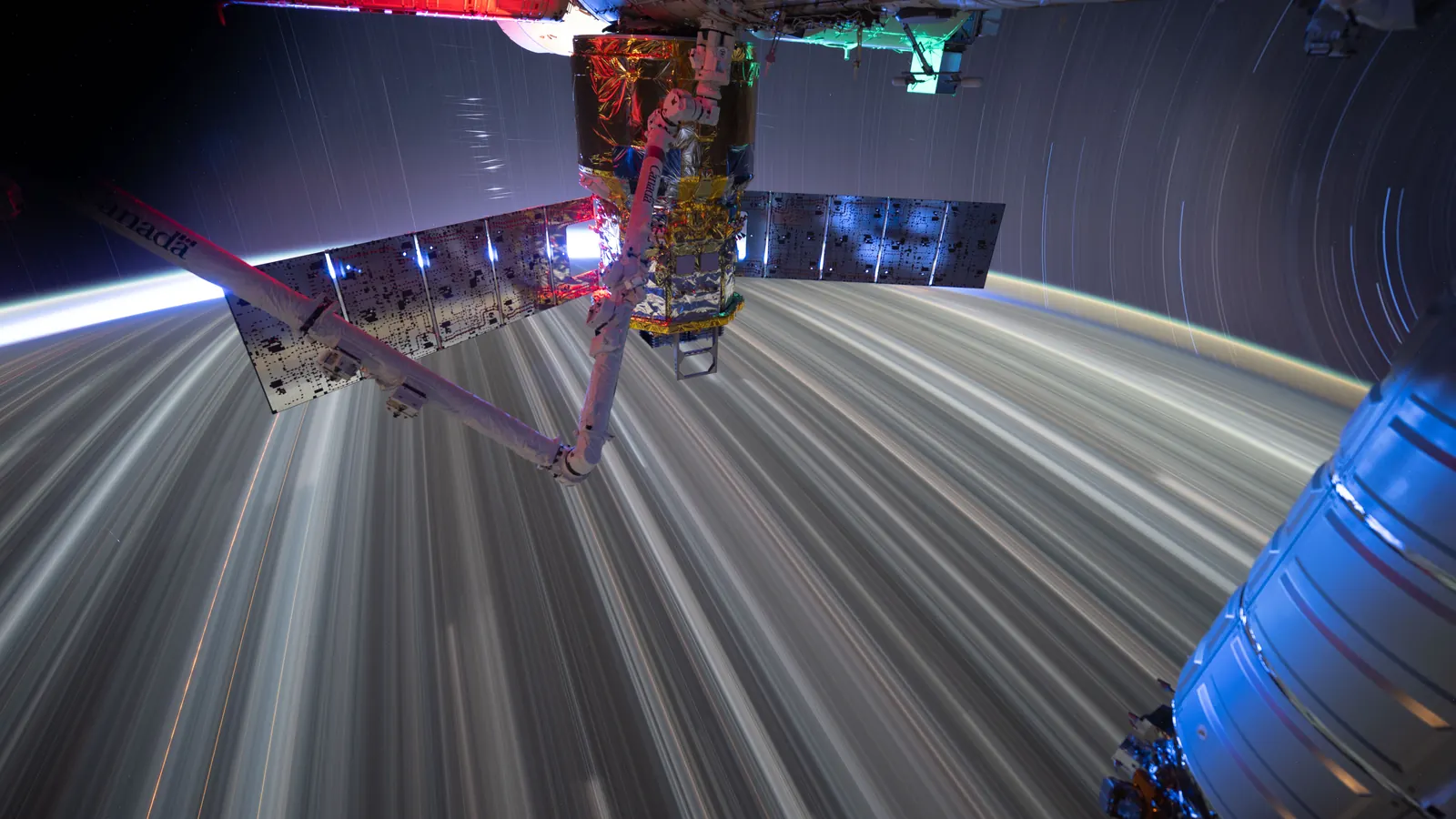 City lights and stars drawn into long streaks in a time exposure taken from the International Space Station as it orbits Earth at night, with station hardware in the foreground