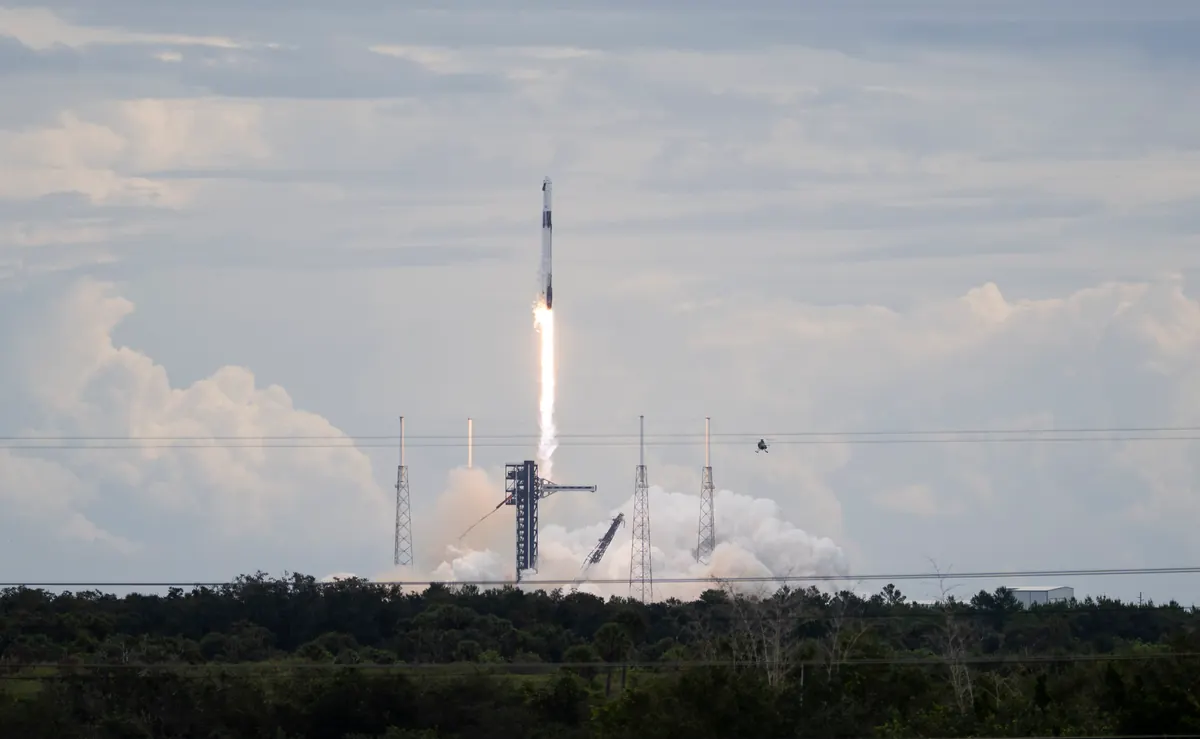 A Falcon 9 rocket climbing on a bright exhaust plume above its launch tower and lightning masts at Cape Canaveral, with steam clouds at the pad and trees in the foreground