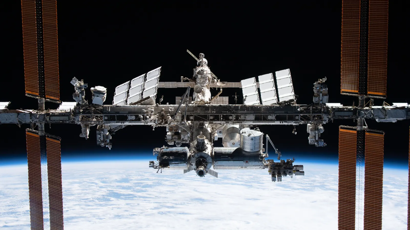 The International Space Station above Earth's horizon, its solar arrays spread wide, photographed from a departing SpaceX Crew Dragon during its flyaround on November 8, 2021