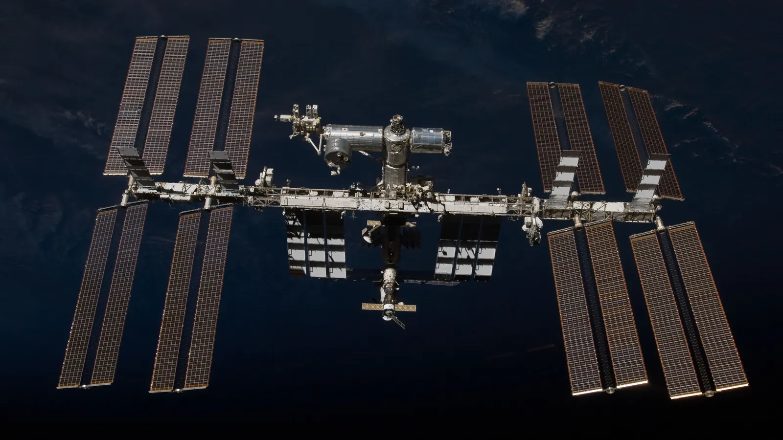 The International Space Station photographed from space shuttle Endeavour after undocking in February 2010, its long truss and eight solar array wings spread over a dark ocean