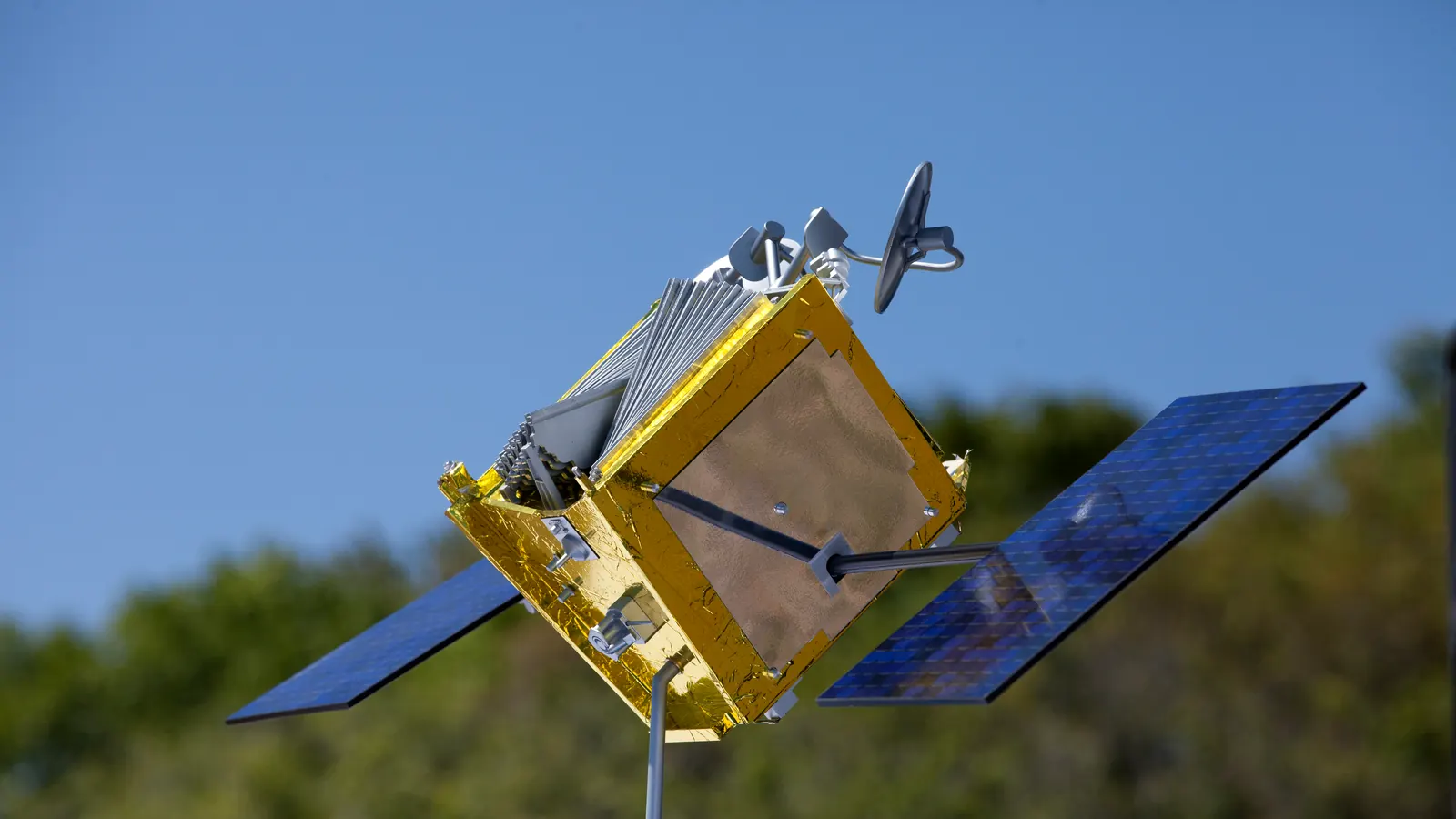 A model of a OneWeb satellite with gold-foil body and two solar panels, displayed outdoors at the March 16, 2017 groundbreaking for the OneWeb Satellites factory at Kennedy Space Center