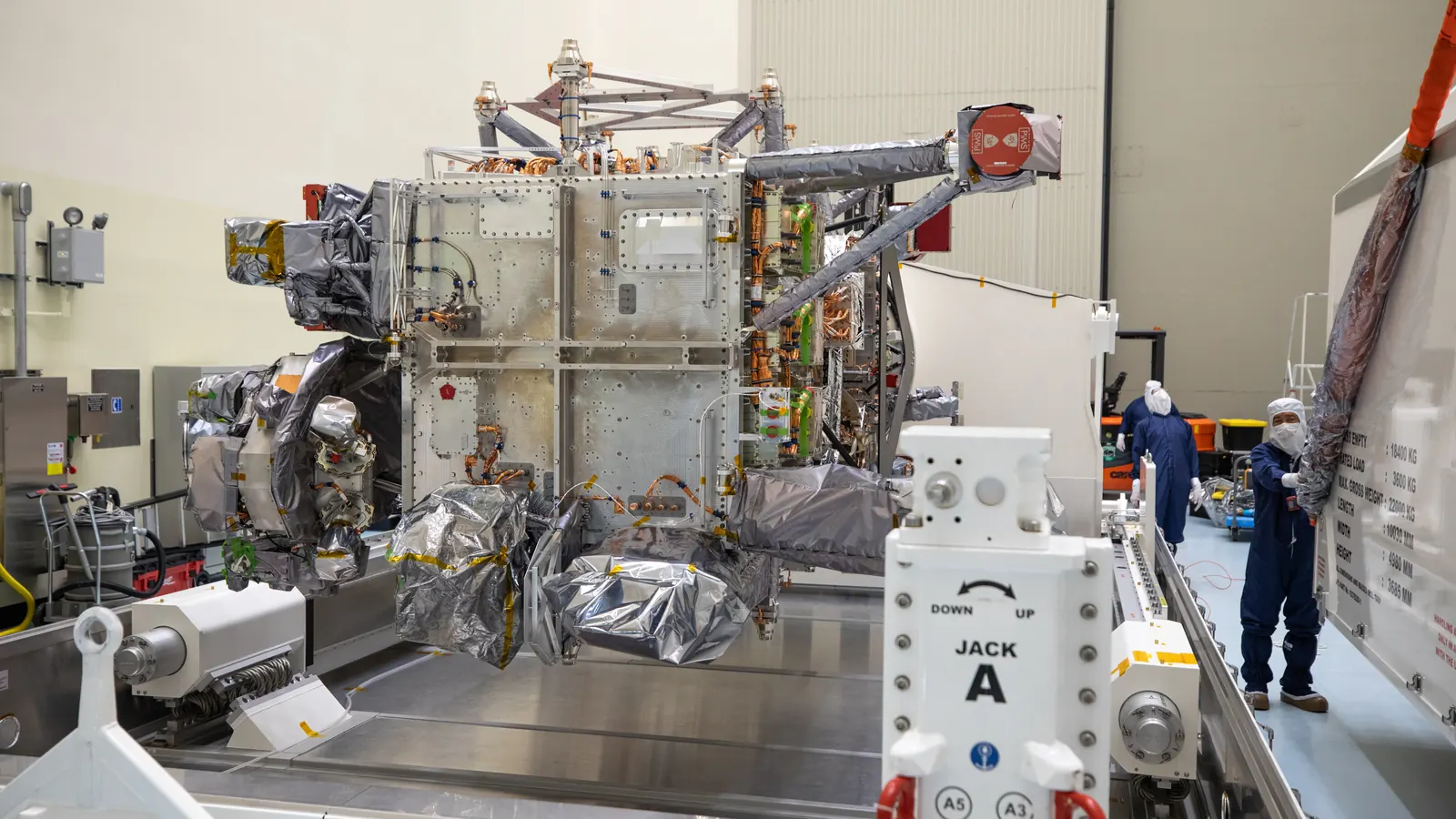 Technicians in cleanroom suits beside NASA's Europa Clipper spacecraft, much of it wrapped in silver insulation, after crews uncrated it in the Payload Hazardous Servicing Facility at Kennedy Space Center on May 28, 2024