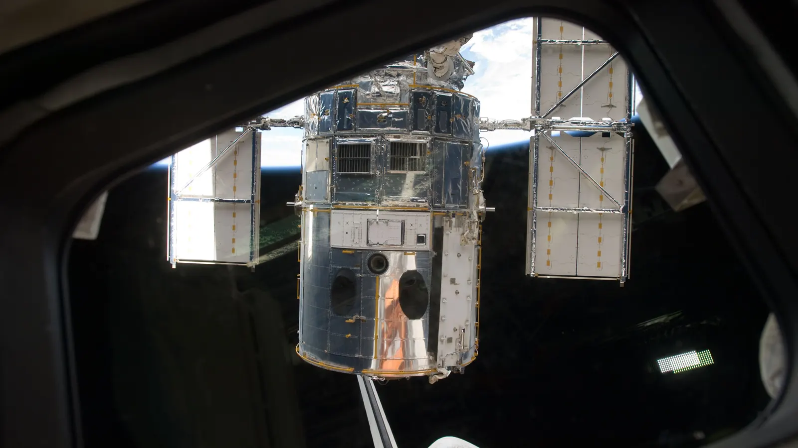 The Hubble Space Telescope held on Atlantis's robotic arm, seen through the shuttle's aft flight deck window before its release in May 2009, with Earth's horizon behind it