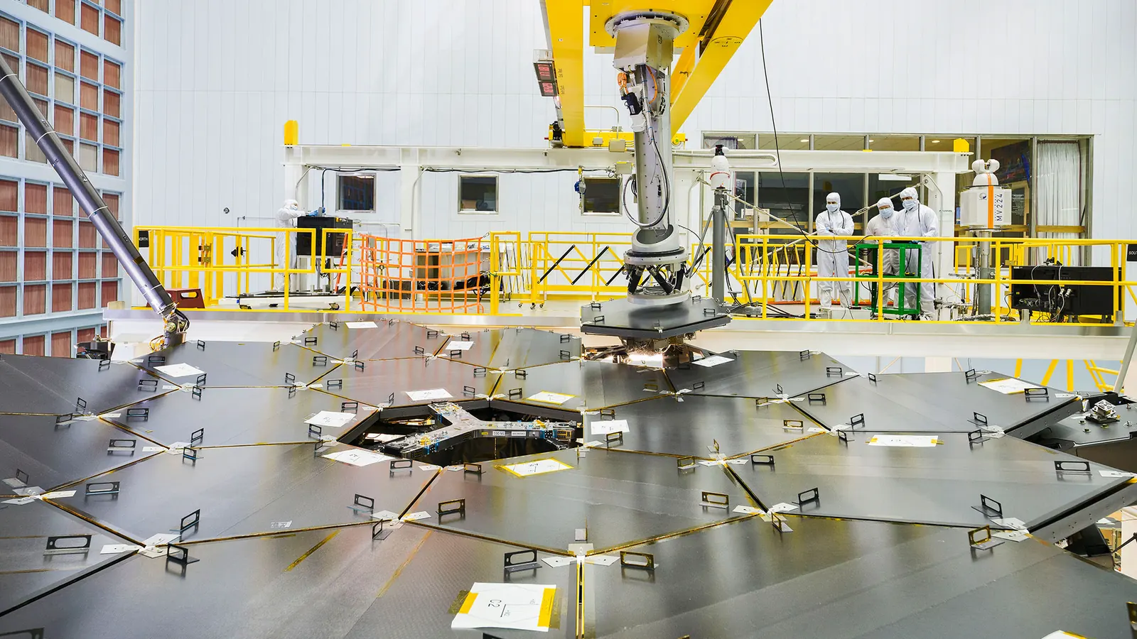 Engineers in cleanroom suits at NASA Goddard watch as the last hexagonal segment is lowered into place on the James Webb Space Telescope's primary mirror in 2017